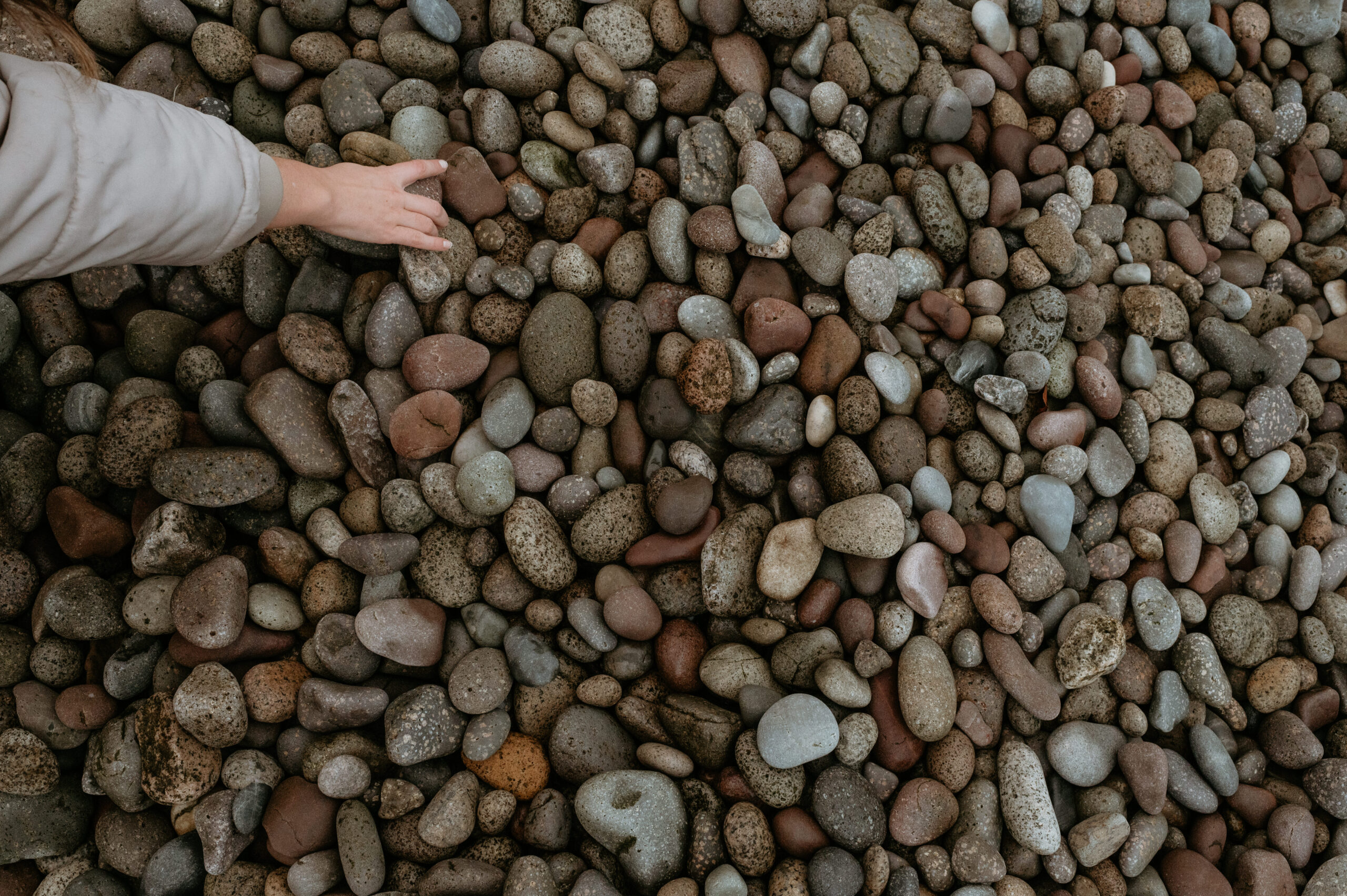 Close up of Raasay pebbled beach with a hand feeling the rocks